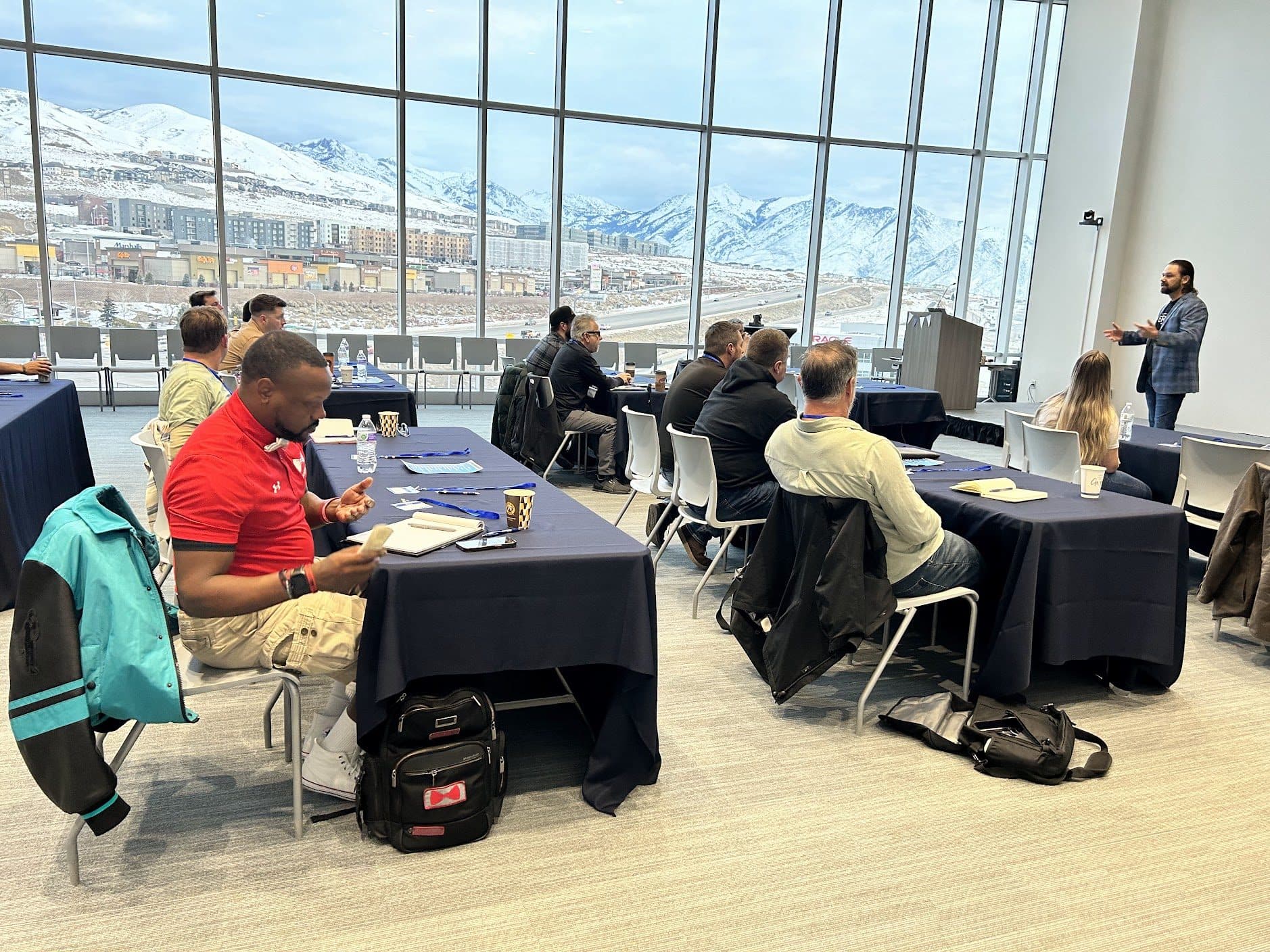 Roofing company owners at a Roofing Academy workshop in a room with floor-to-ceiling windows and snow-covered mountains outside.